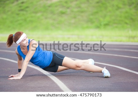 Caucasian Sportswoman in Professional Sportsgear Having Body Stretching Exercises On Sport Venue Outdoors. Horizontal Image