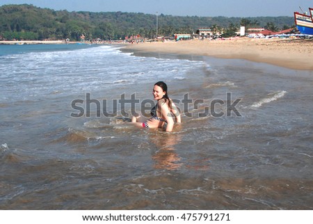 Happy beautiful girl in a bikini is sitting on the beach at the water's edge 