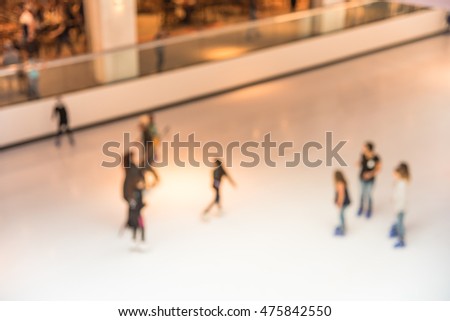 Top view blurred motion background of parents and kids play indoor ice skating in modern shopping mall. Defocused of indoor ice skating with people on the ice rink. Natural light from glass roof.