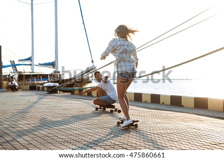 Young beautiful couple walking at seaside, skateboarding.