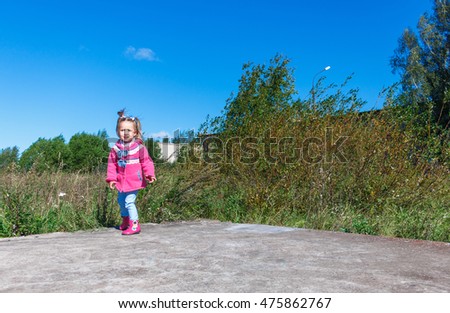 Little girl in a pink coat, jeans and pink boots walking in the park.