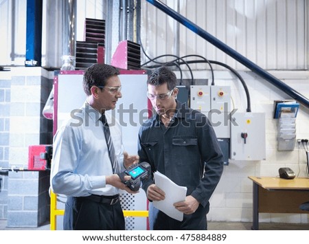 Office manager and worker discuss energy use with infra red camera next to boiler in factory
