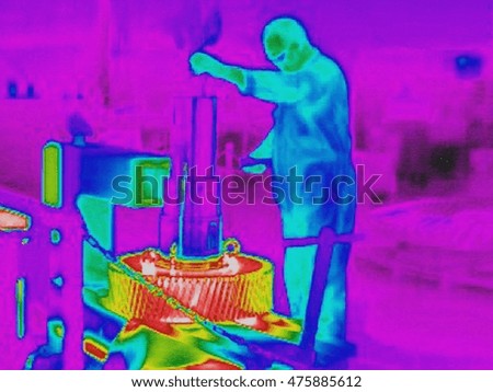 Infra red heat image of worker fitting cold shaft into hot gears in factory