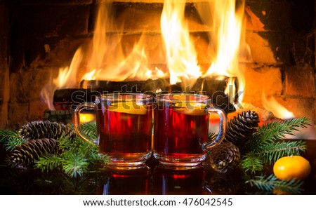Christmas New Year composition. Two glasses of mulled red wine or hot drink tea with christmas decoration - fir branches in front of warm fireplace. Romantic, relaxed magical atmosphere near fireplace
