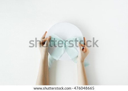 white gift cardboard box with blue bow and girl's hands on white background. flat lat, top view