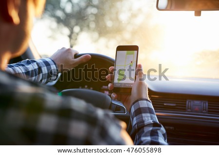 Man in plaid shirt sitting in the car and holding black mobile phone with map gps navigation, toned at sunset. Royalty-Free Stock Photo #476055898
