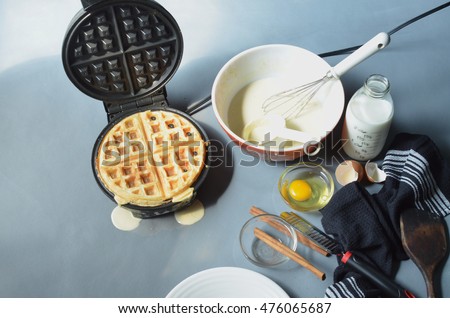 making waffles at home--waffle iron, batter in bowl, ingredients, cooking utensils Royalty-Free Stock Photo #476065687