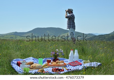 Man with hat observing landscape with binoculars on picnic with hills in background