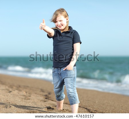 Young girl with shirt and blue jeans is showing thumbs up on the beach; shallow depth of field