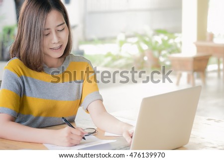 Woman smiling and hand hold pen point stock market chart and use laptop in coffee shop. vintage effect.