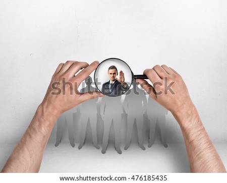 Close-up view of a man's hands focusing magnifier on a businessman with his hand raised. Body language. Stop sign. Employment issues. Royalty-Free Stock Photo #476185435