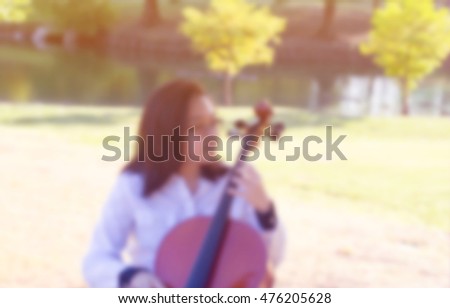 a blurry picture of teen girl playing cello in green park, filtered color tone