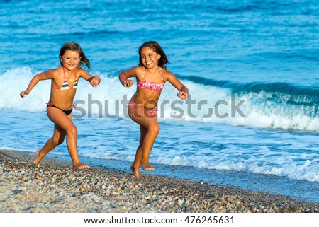 Close up action portrait of two young girls running together on pebble beach.