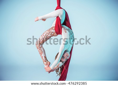 Graceful gymnast performing aerial exercise with red fabrics on blue background