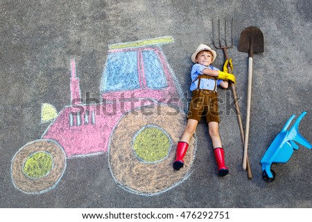 Happy little kid boy in straw hat and rain boots having fun with tractor picture drawing with colorful chalks. Children, lifestyle, fun concept. child dreaming of future and profession.