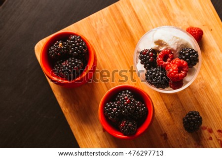 Blackberry ice cream in a cup and a glass on a background of wooden boards and a blurred green.