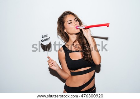 Young brunette girl in bikini sitting and blowing in whistle over white background