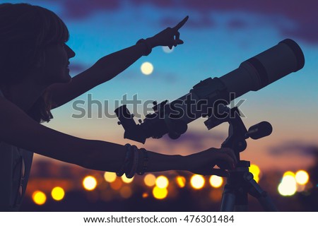 Girl looking at the stars with telescope beside her and de-focused city lights. Royalty-Free Stock Photo #476301484