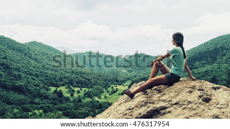 Young woman resting on peak of cliff and enjoying view of valley in summer