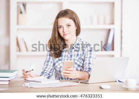 Cute young businesswoman using smartphone at workplace