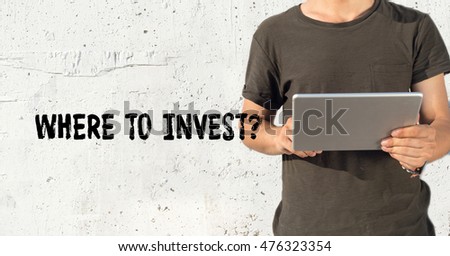 Young man using tablet pc and WHERE TO INVEST? concept on wall background