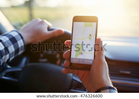Man in the car and holding black mobile phone with map gps navigation, toned at sunset. Royalty-Free Stock Photo #476326600