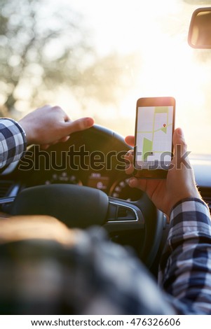 Man in plaid shirt sitting in the car and holding black mobile phone with map gps navigation, toned at sunset.
