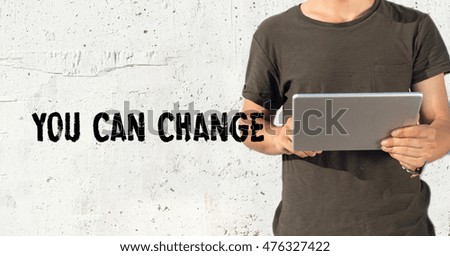 Young man using tablet pc and YOU CAN CHANGE concept on wall background