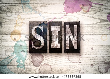 The word "SIN" written in vintage, dirty metal letterpress type on a whitewashed wooden background with ink and paint stains.