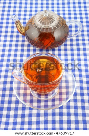 Glass cup of tea and teapot on tablecloth