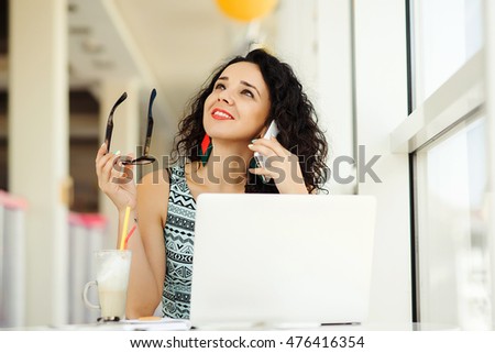 Smiling beautiful young woman using laptop and talking on the mobile phone.
