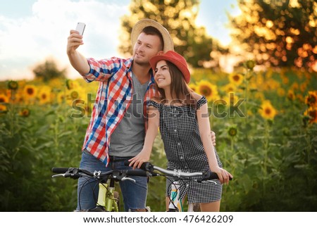 Young couple on bicycles taking photo in field