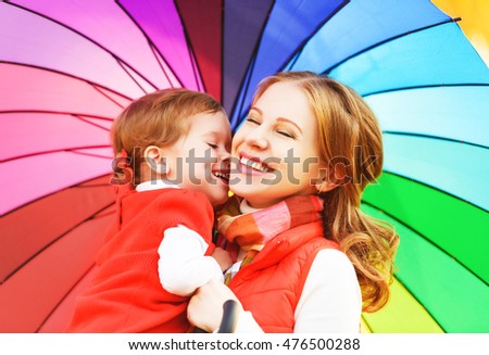 Happy family mum and child daughter with rainbow colored umbrella under rain on nature