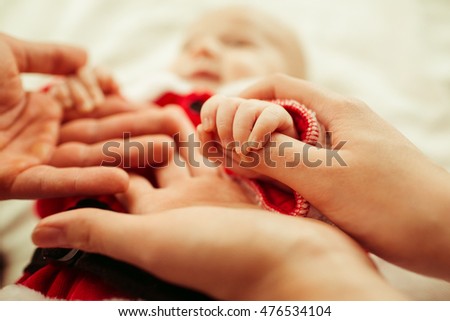 Tiny palms of little boy in red suit lie in parents hands
