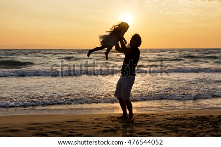 Silhouette of a happy father and daughter on the beach at sunset