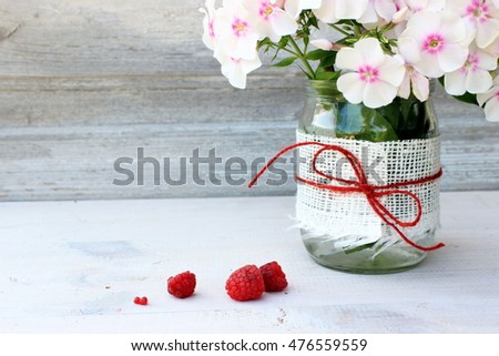 Romantic card with bunch of flowers / phlox in a glass vase decorated with pure white burlap and bright red jute bow. Full light floral composition. Rustic style of home decor