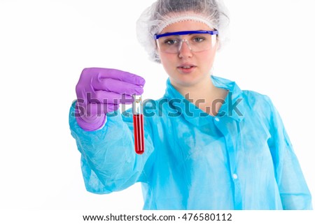 The woman in a blue protective coat with protective glasses  is showing a tube with red liquid on a white background.