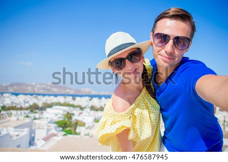 Selfie couple taking pictures at Mykonos island, Cyclades. Tourists people taking travel photos with smartphone on summer holidays.