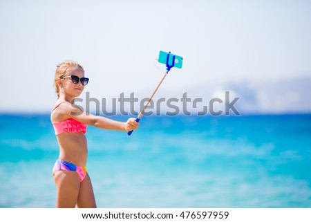 Little girl taking selfportrait by her smartphone on the beach. Kid enjoying her suumer vacation and making photos for memory