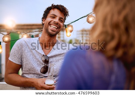 Multi-ethnic millennial couple flirting while having a drink on rooftop terrasse at sunset Royalty-Free Stock Photo #476599603