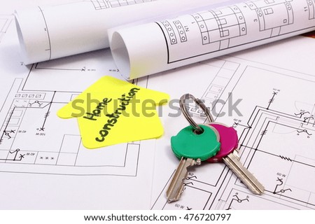 Home keys, house of yellow paper with text home construction and rolls of diagrams lying on electrical construction drawing of house, concept of building home