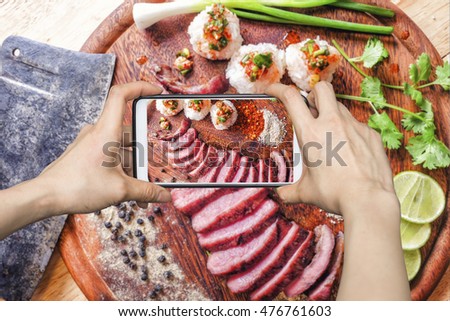 Girl taking pictures on mobile smart phone a Thai style BBQ grill Meat and Sticky rice with spicy sauce