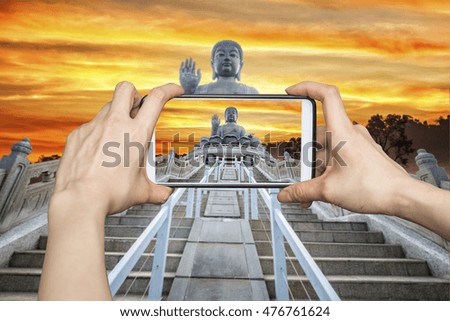 Girl taking pictures on mobile smart phone in Front View of Tian Tan Giant Buddha in golden sky