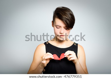 Heart-broken. short-haired girl tearing a heart - symbol of love and health, close-up, isolated on a gray background