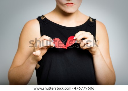 Heart-broken. short-haired girl tearing a heart - symbol of love and health, close-up, isolated on a gray background
