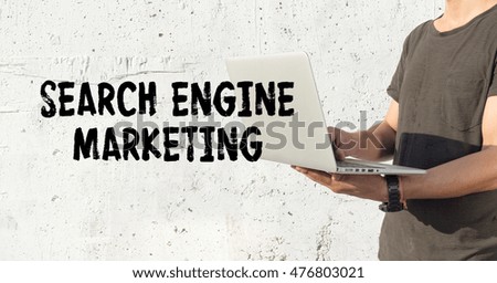 Young man using laptop and SEARCH ENGINE MARKETING concept on wall background