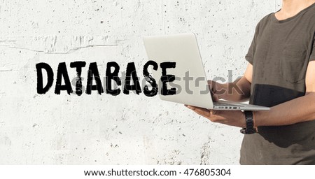 Young man using laptop and DATABASE concept on wall background