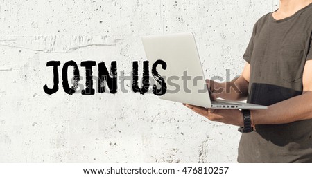 Young man using laptop and JOIN US concept on wall background