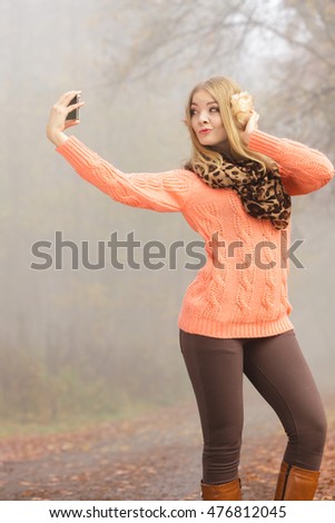 Lovely fashion woman in fall autumn park taking selfie self photo picture. Pretty cute young girl in sweater pullover and earmuffs photographing.