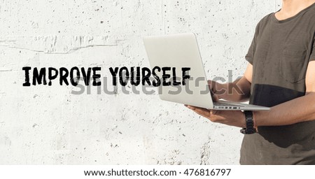 Young man using laptop and IMPROVE YOURSELF concept on wall background
